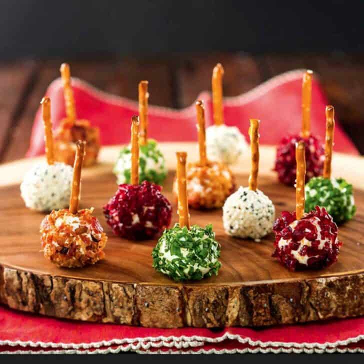 A dozen assorted mini cheese balls on a wooden platter.