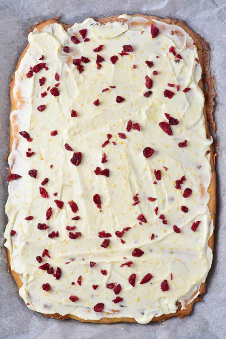 Uncut cookie bars spread with frosting and topped with cranberries.