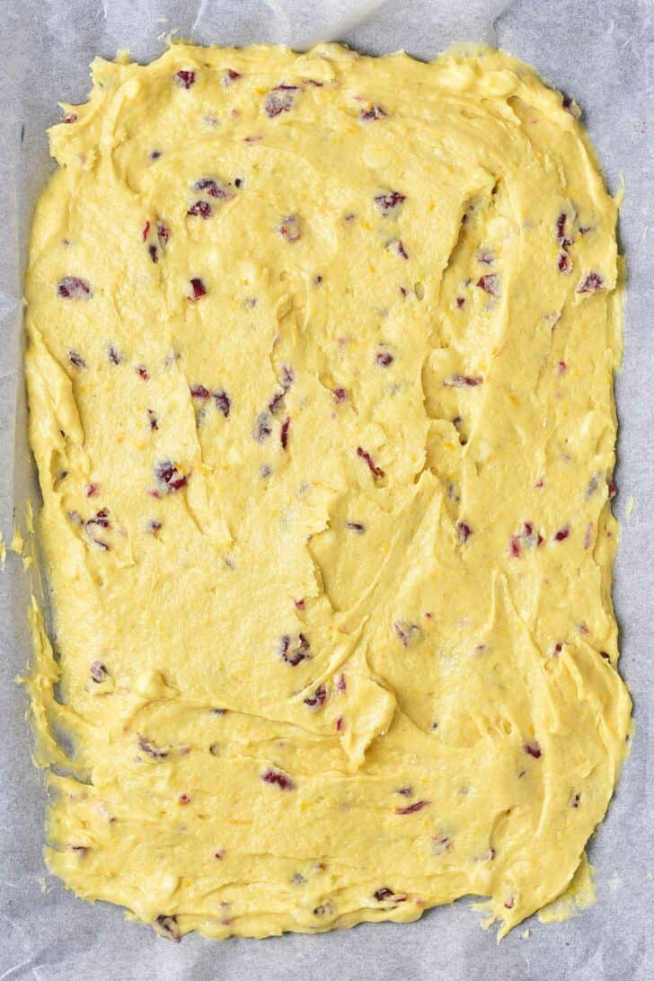 Uncooked cookie dough spread in a baking pan on parchment paper.