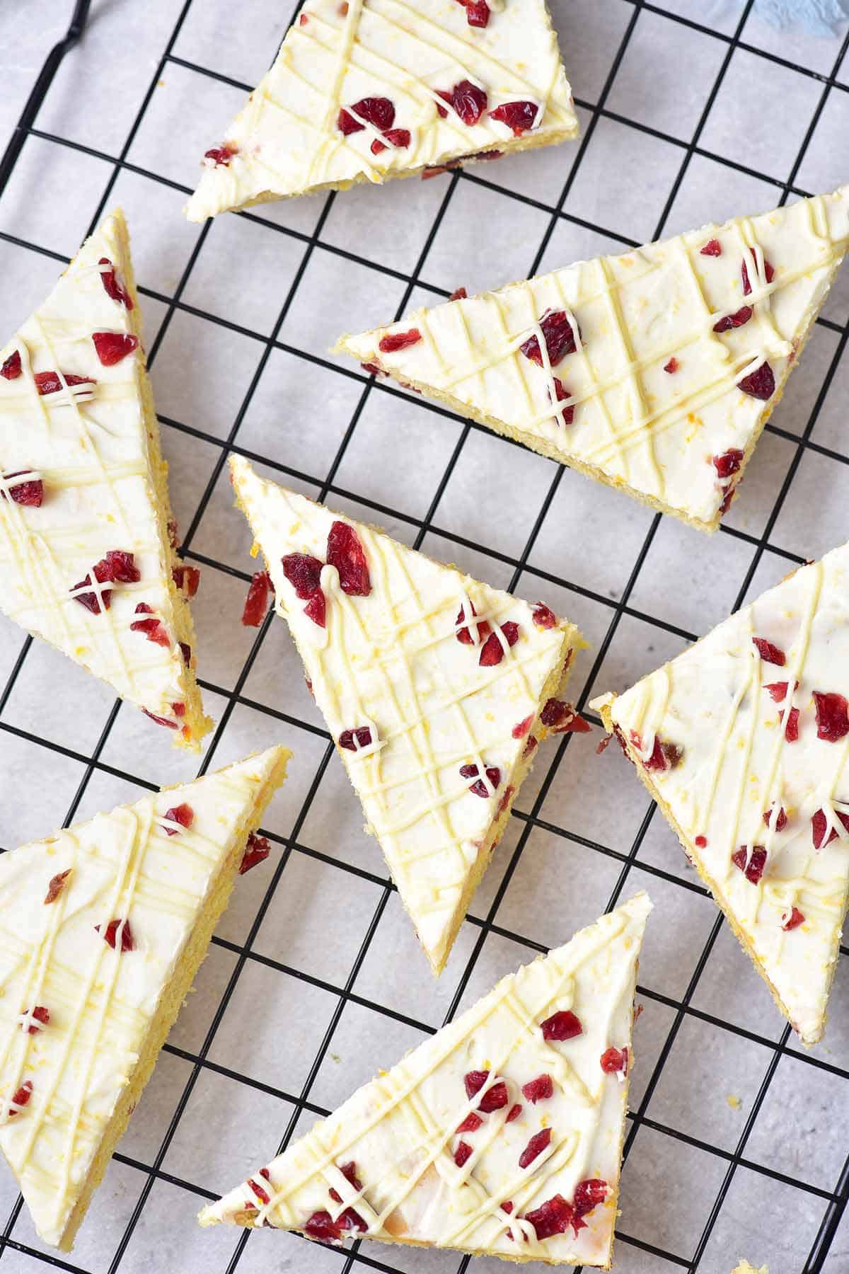 Seven cranberry bars drizzled with white chocolate on a cooling rack.