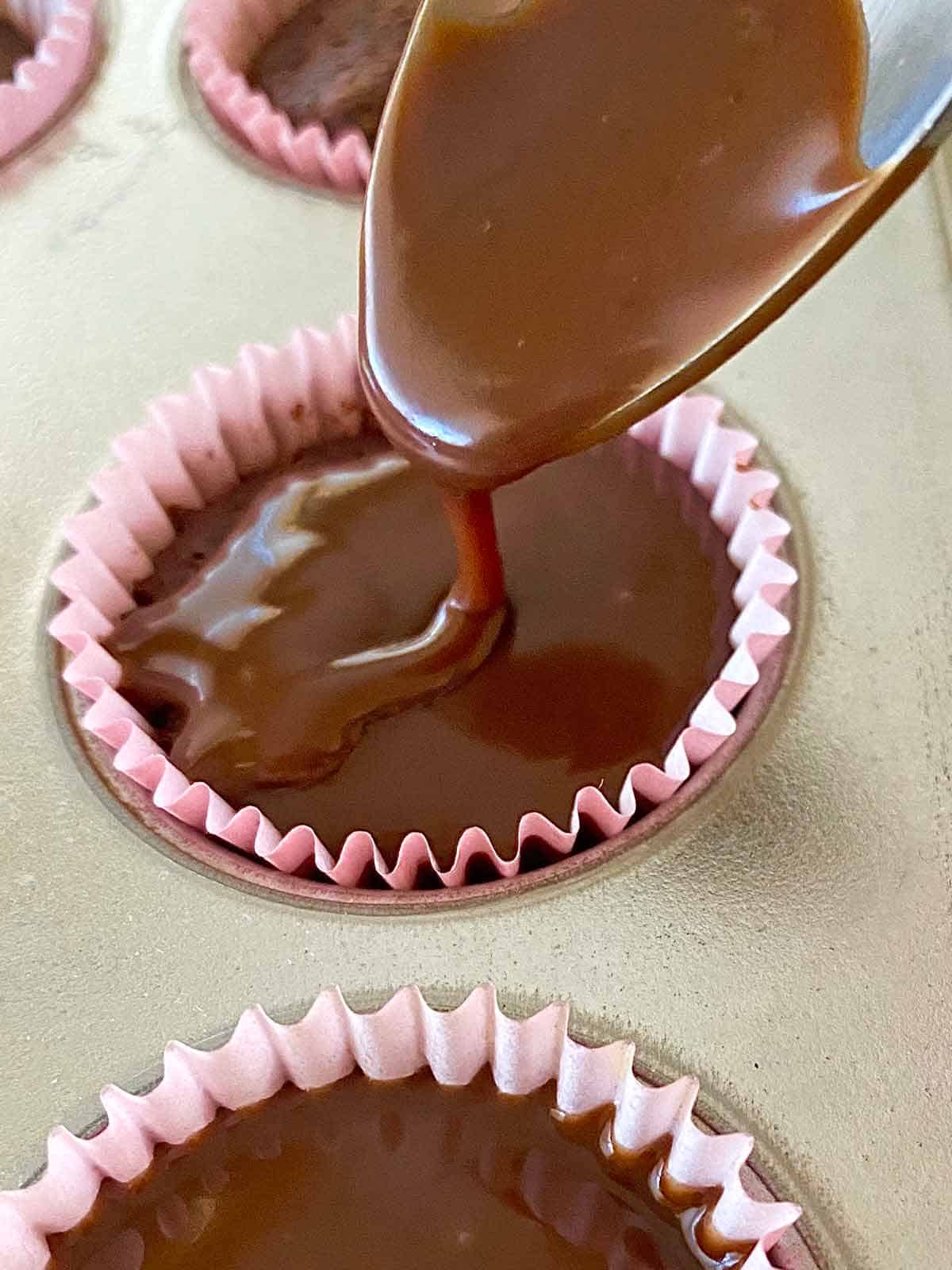 Using a spoon to pour chocolate ganache glaze on a small cake.