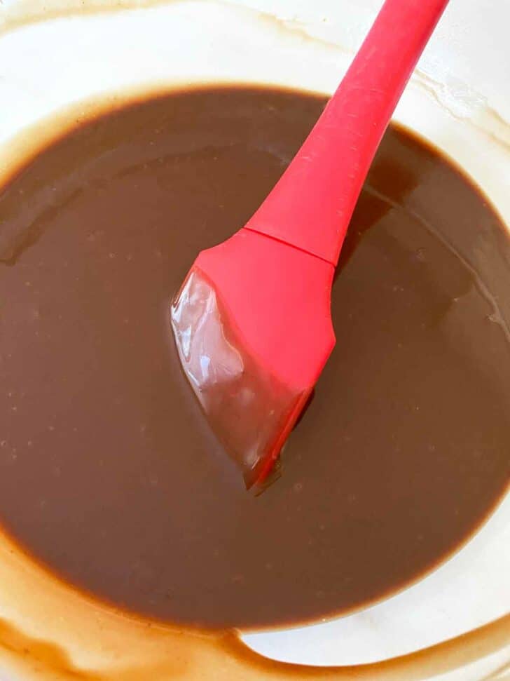 Stirring chocolate ganache frosting with a red spatula.