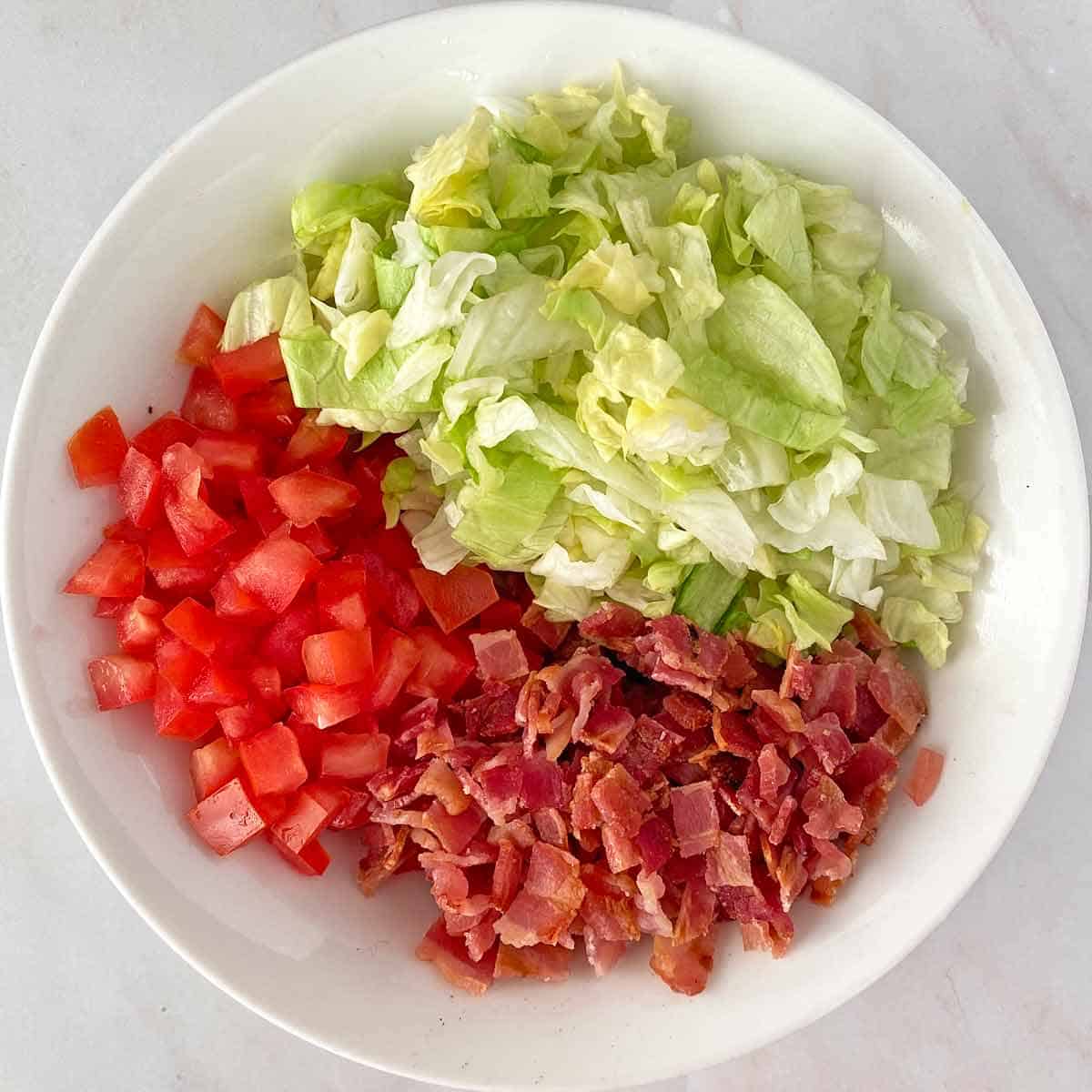 Chopped bacon, lettuce and tomato in a white bowl.
