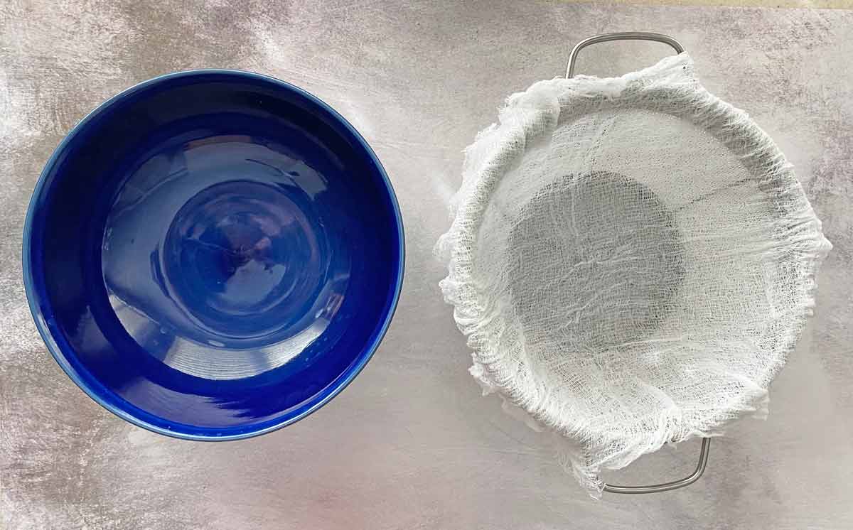 A blue bowl and a strainer lined with cheesecloth.
