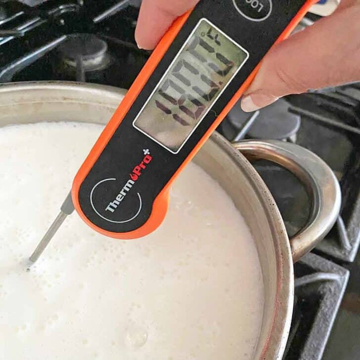 Instant read thermometer being placed in a saucepan of hot milk.