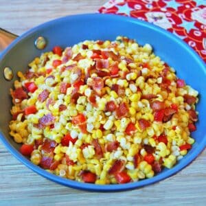 A large skillet filled with fried corn with bacon and chopped red bell peppers.