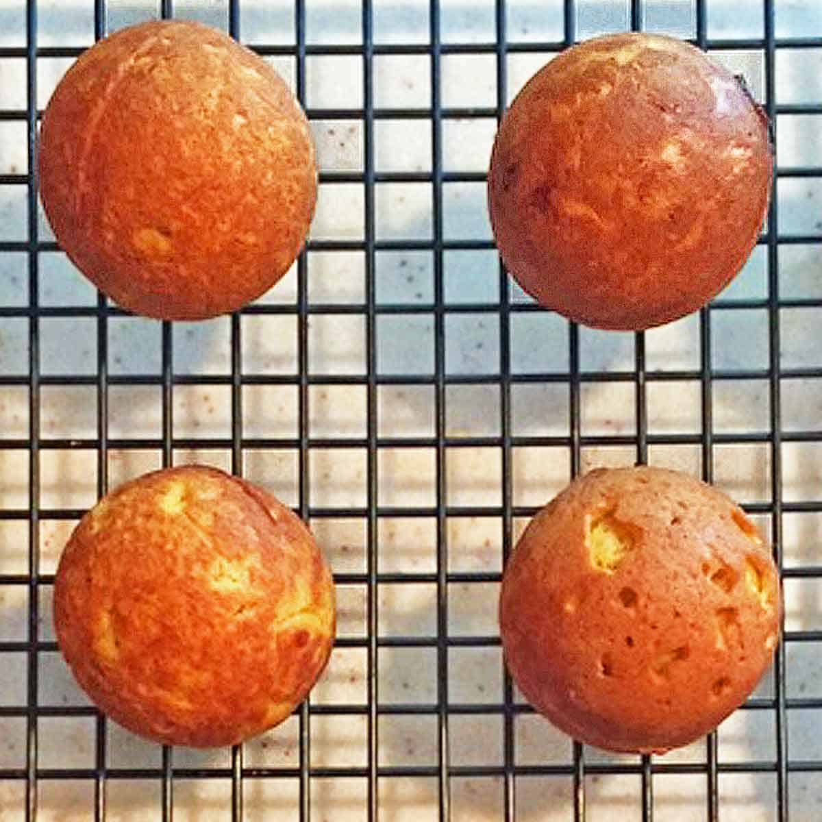 Four baked pumpkin donut holes up close on a cooling rack.