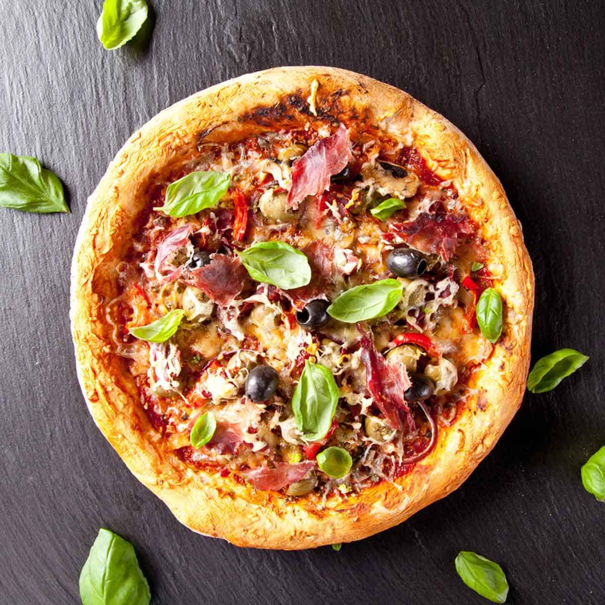 A homemade pizza topped with meats, veggies, and fresh basil leaves.