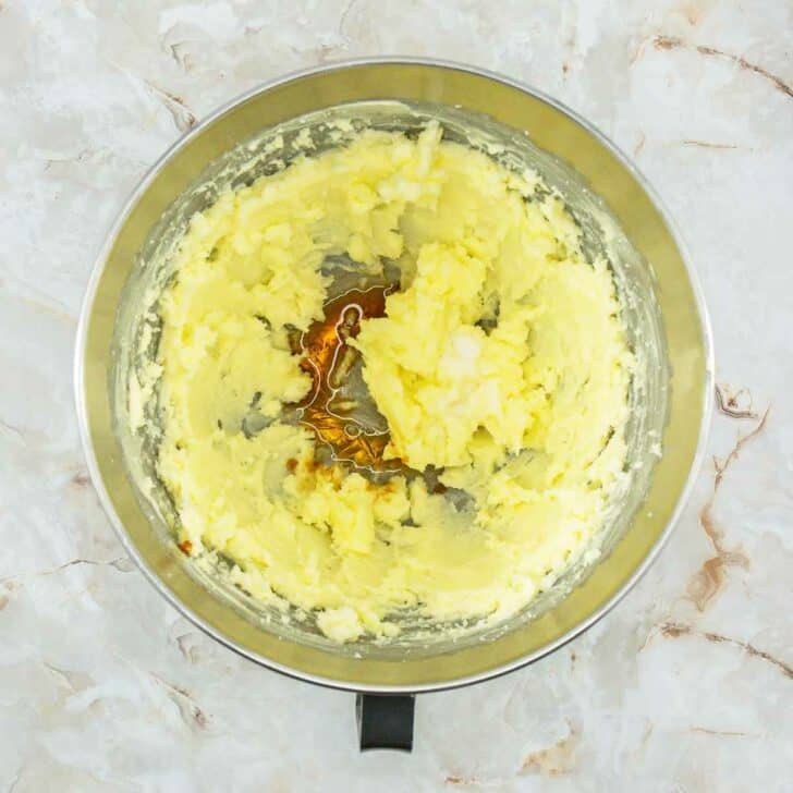 A mixing bowl with creamed butter, vanilla and almond extract.