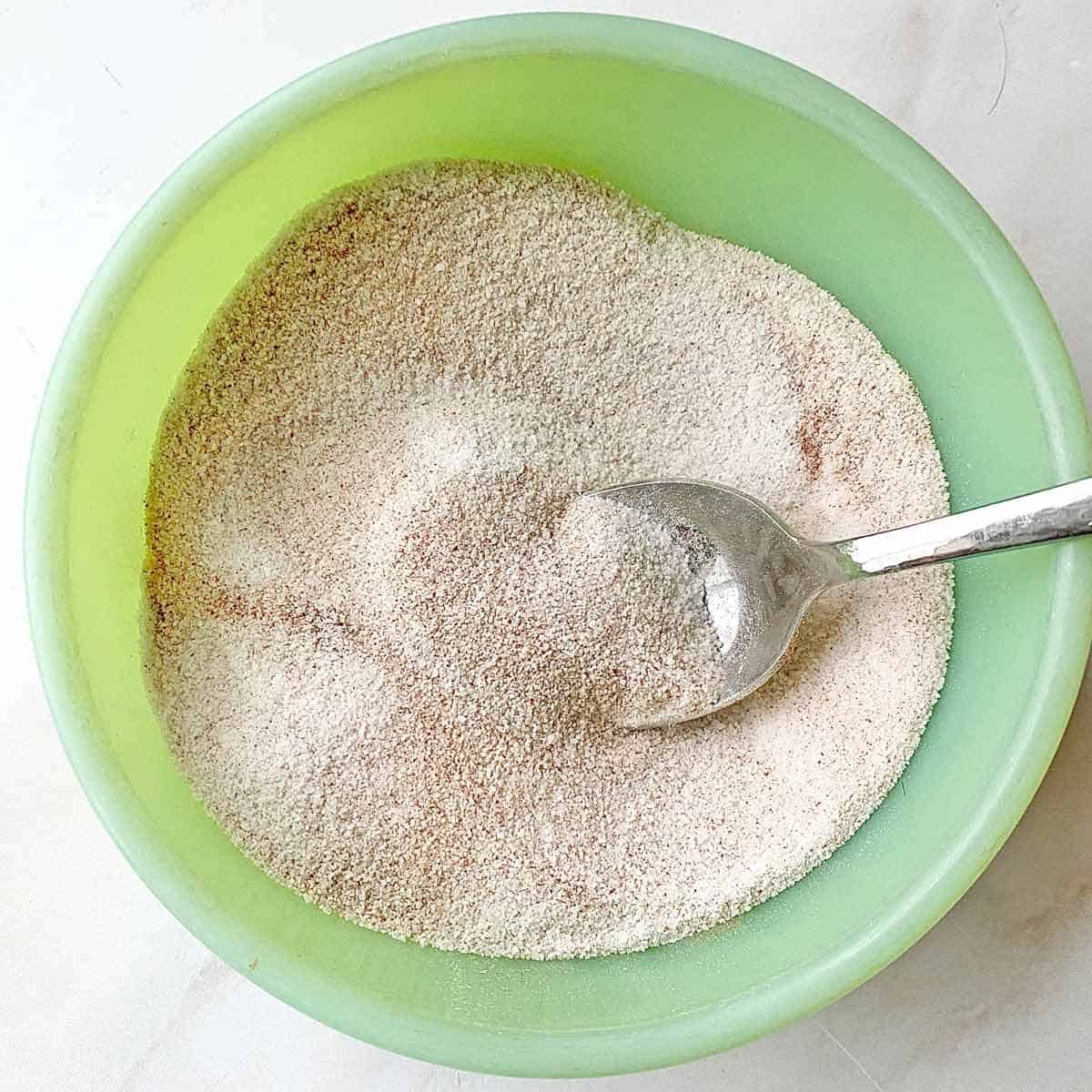 Stirring cinnamon and sugar together in a small green bowl with a spoon.