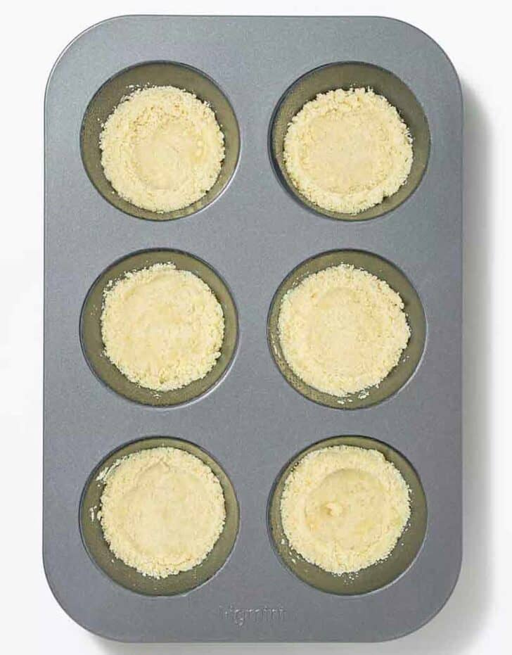 A nonstick muffin tin filled with cookie crumb mixture.
