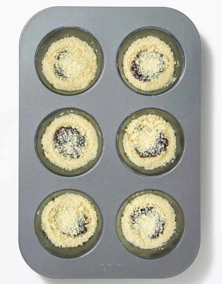 Jam and cookie crumb mixture in a muffin tin, ready to bake.