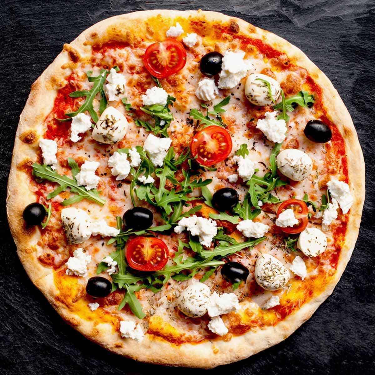 A large homemade pizza with tomatoes, olives and fresh mozzarella cheese.