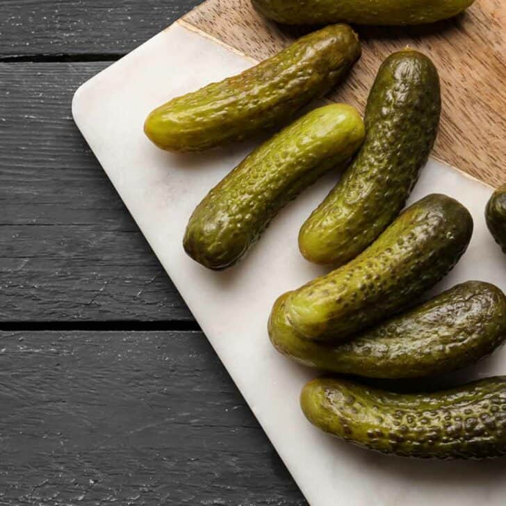 Six dill pickles on a cutting board.