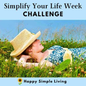 A woman in a blue floral dress and straw hat lies on her back in a grassy field with wildflowers, hands behind her head. Text above reads Simplify Your Life Week Challenge with Happy Simple Living and a sunflower icon below.