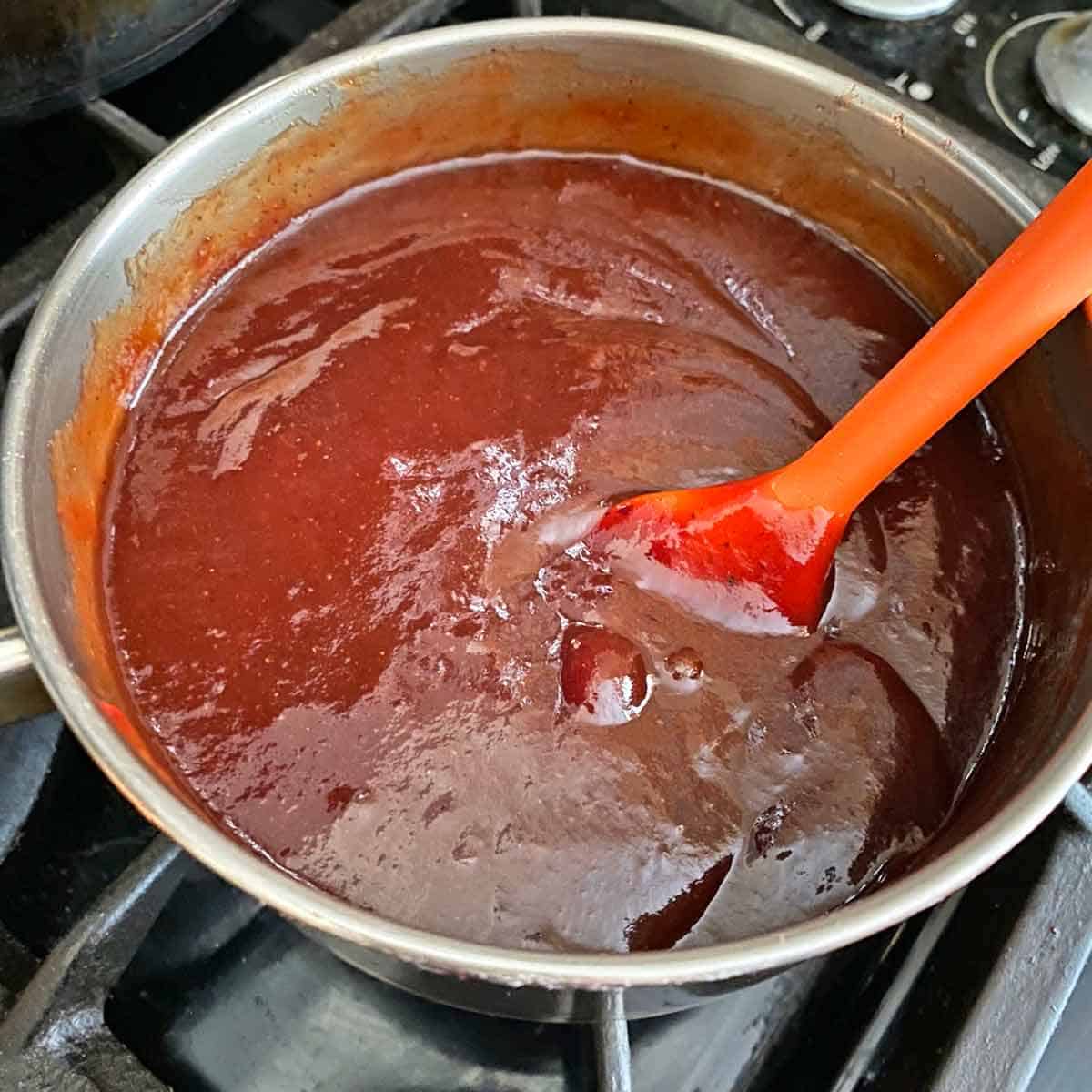 Stirring barbecue sauce and cranberry sauce in a saucepan.