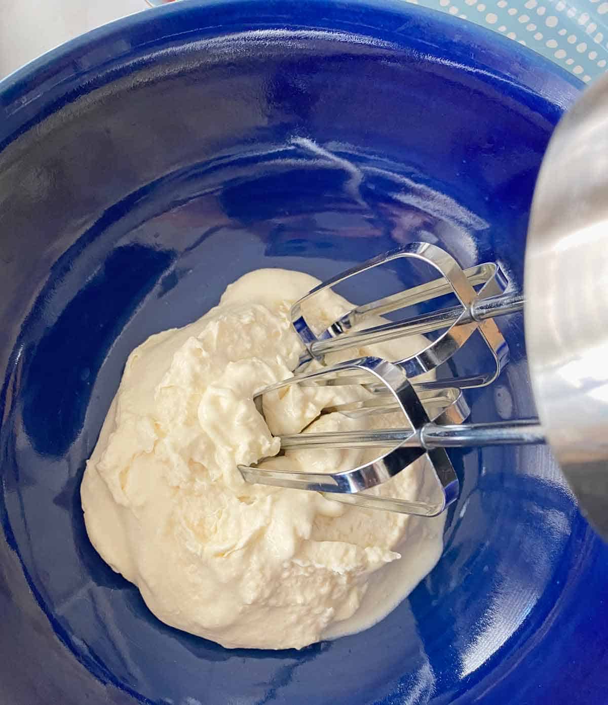An electric mixer beating Parmesan cream mixture in a blue bowl.