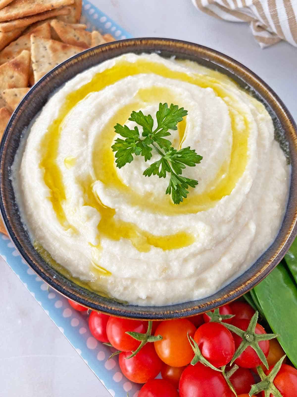 Whipped ricotta cheese dip in a bowl topped with olive oil and served with crackers and crudites.