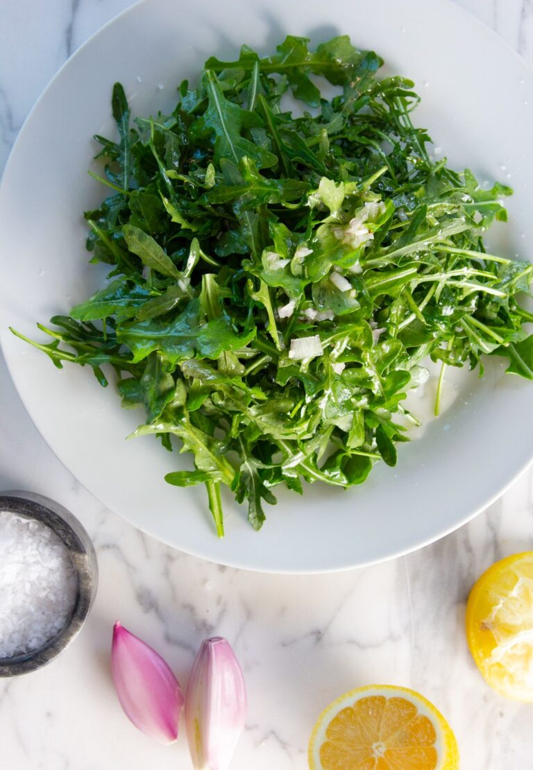 Arugula salad on a white plate with lemon and garlic.