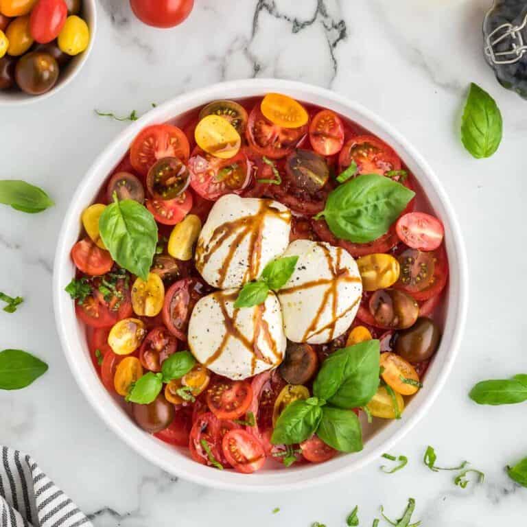 A salad of cherry tomatoes, burrata cheese, and basil leaves.