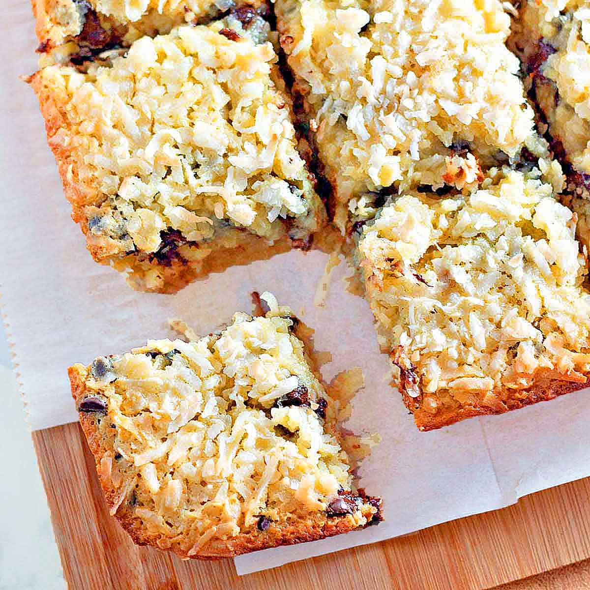 Four coconut chocolate chip cookie bars on a wood cutting board.