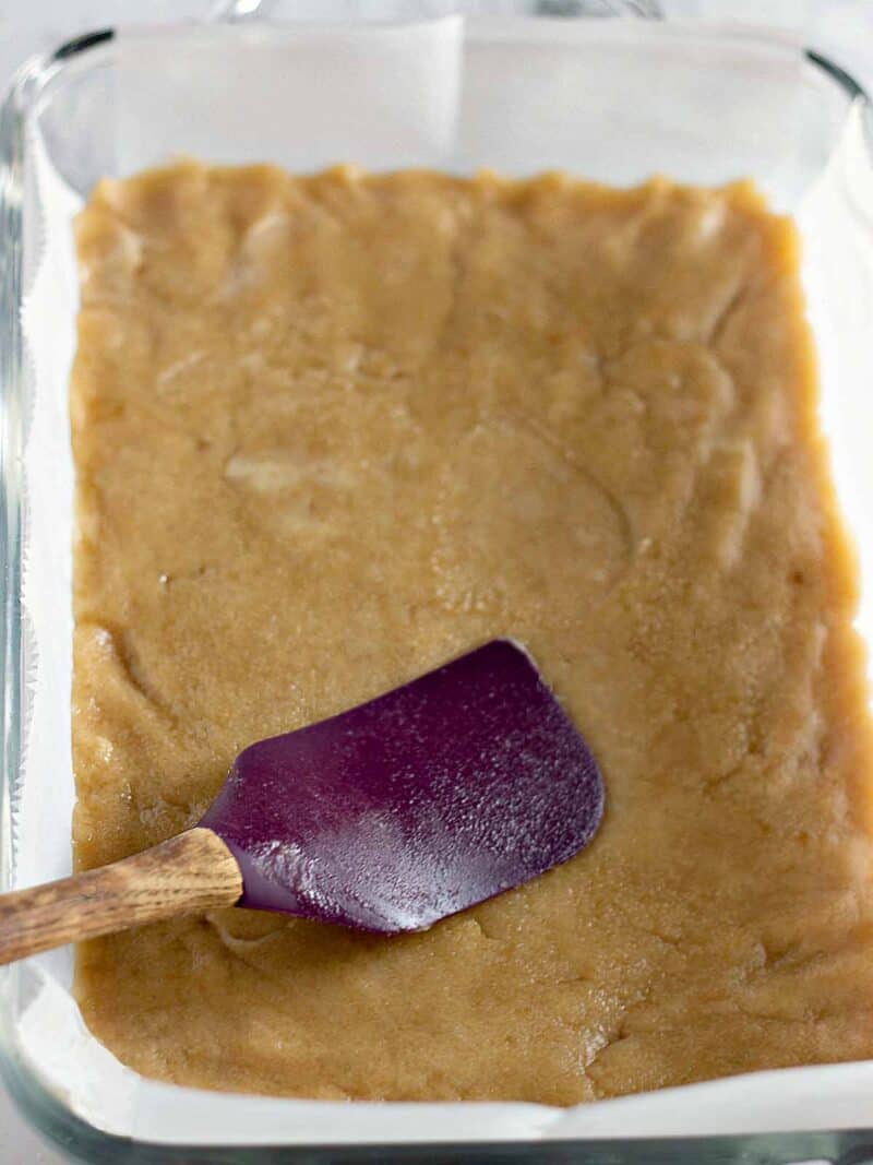 Pressing the cookie dough mixture into the bottom of a parchment lined baking dish.