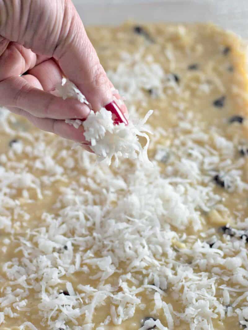 Sprinkling more coconut on the top of the coconut chocolate chip bars before baking.
