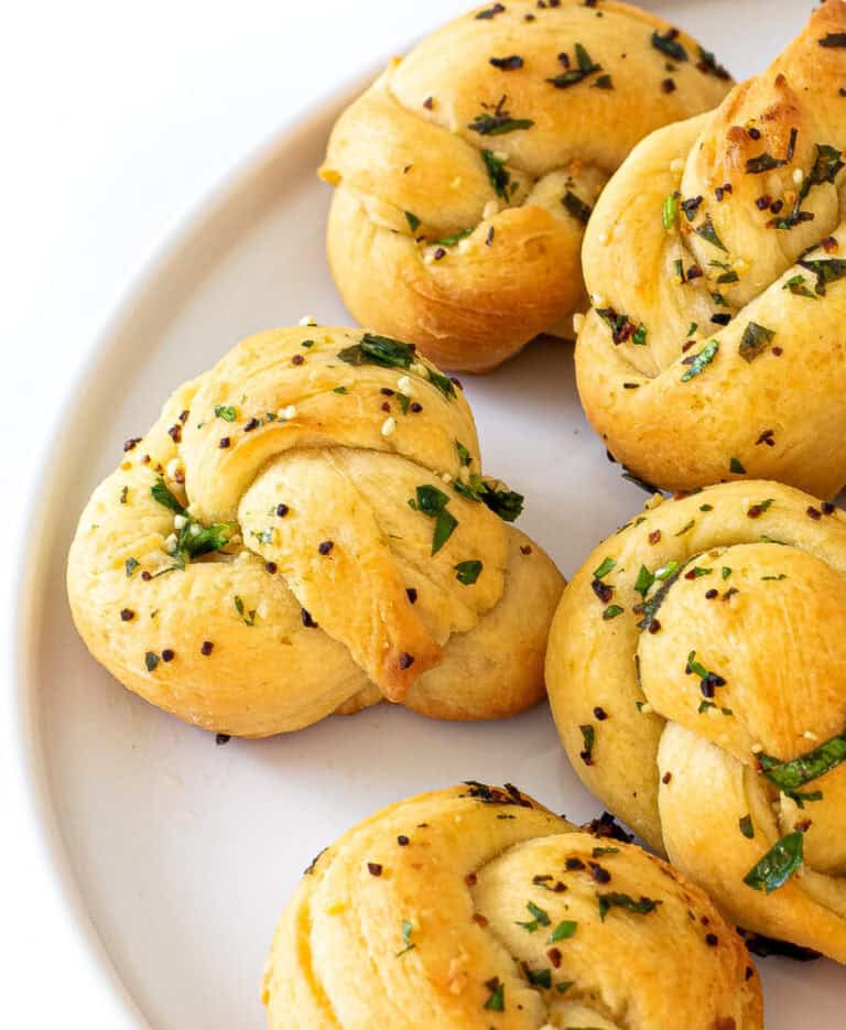 Five garlic knots on a white plate.
