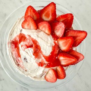 Fresh strawberry halves and strawberry preserves topping a bowl of cheesecake dip.