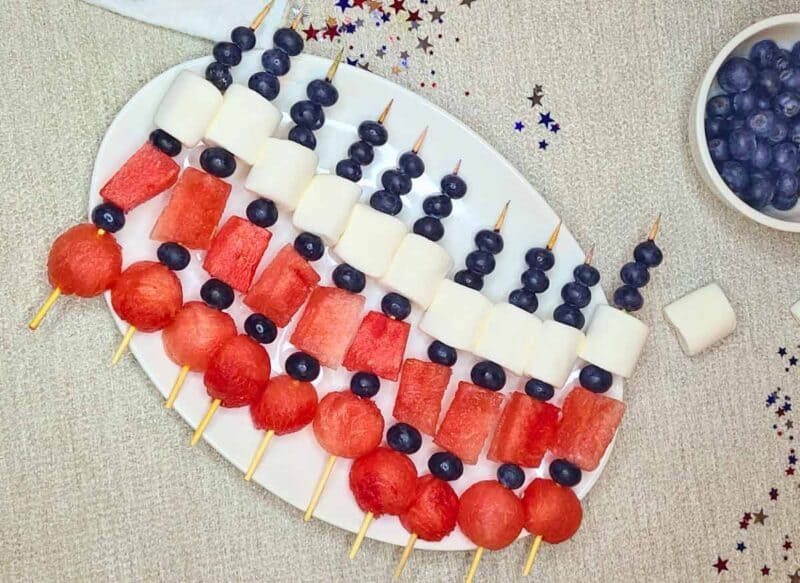 Assembling fruit skewers with blueberries, marshmallows, and watermelon balls and cubes.