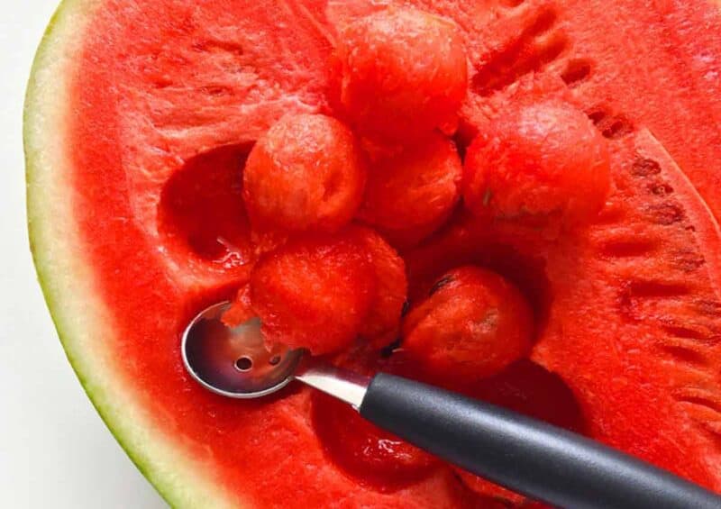 Using a melon baller to make watermelon balls.