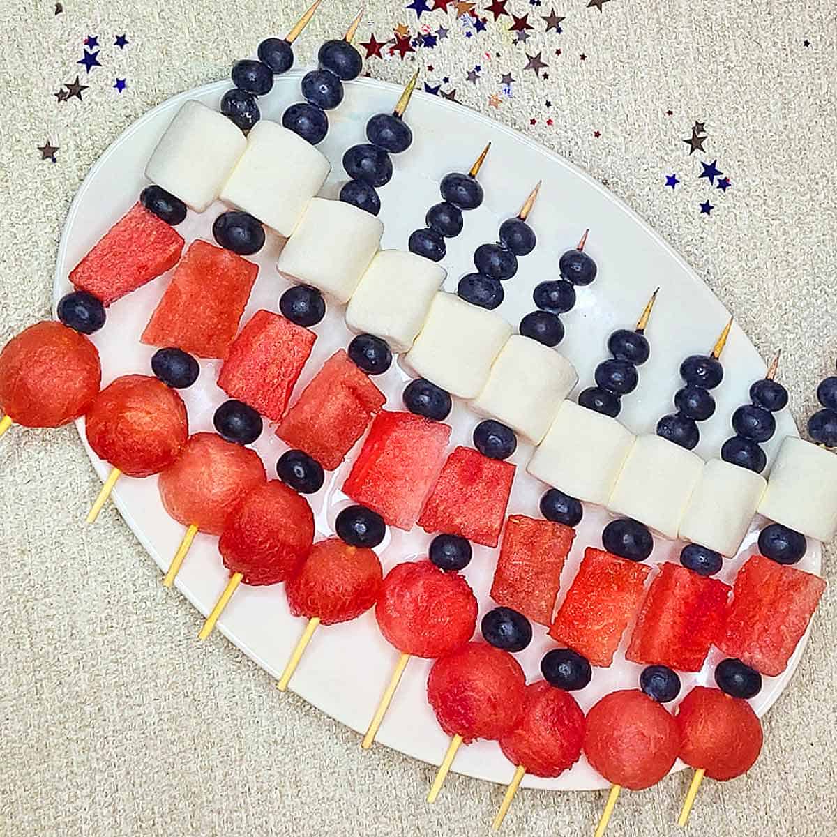 Ten red white and blue fruit skewers on a white serving platter.