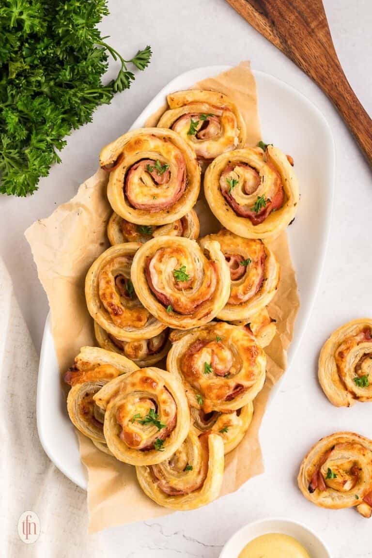 A dozen ham and cheese pinwheels on a white serving dish.