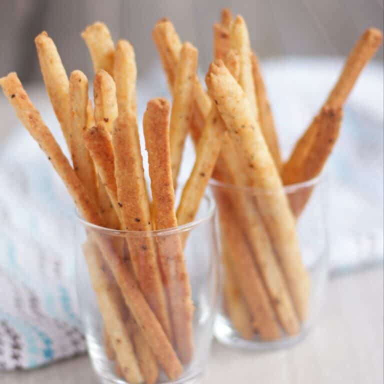 Cheese straws in two glasses sitting on a table.