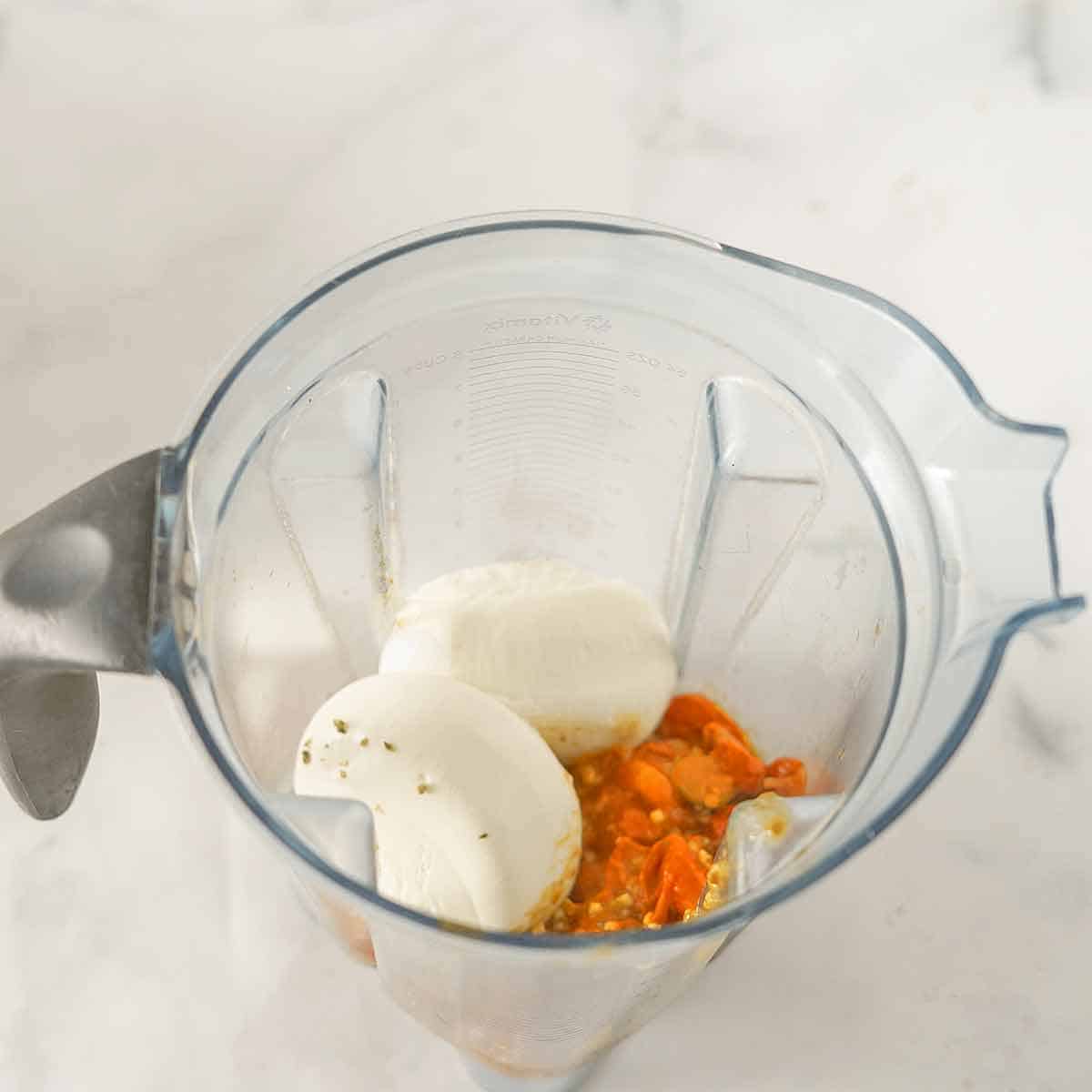 Cooked tomatoes and two balls of burrata cheese in a blender.