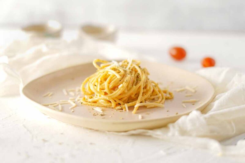 Spaghetti noodles topped with burrata cheese sauce, with cherry tomatoes in the background.