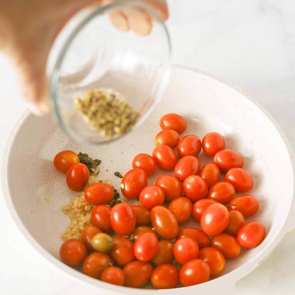 Adding seasonings to the skillet with cherry tomatoes.