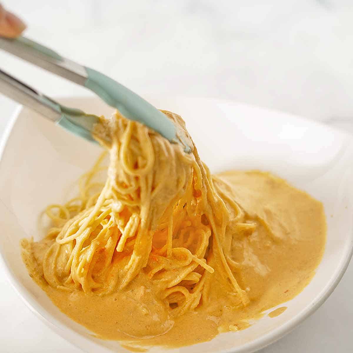Tossing the sauce and hot spaghetti noodles in a bowl with tongs.