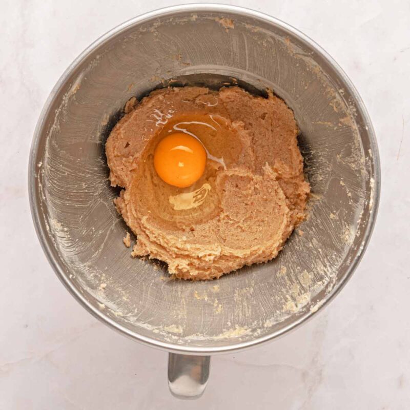 Adding eggs to the cookie dough in a mixing bowl.