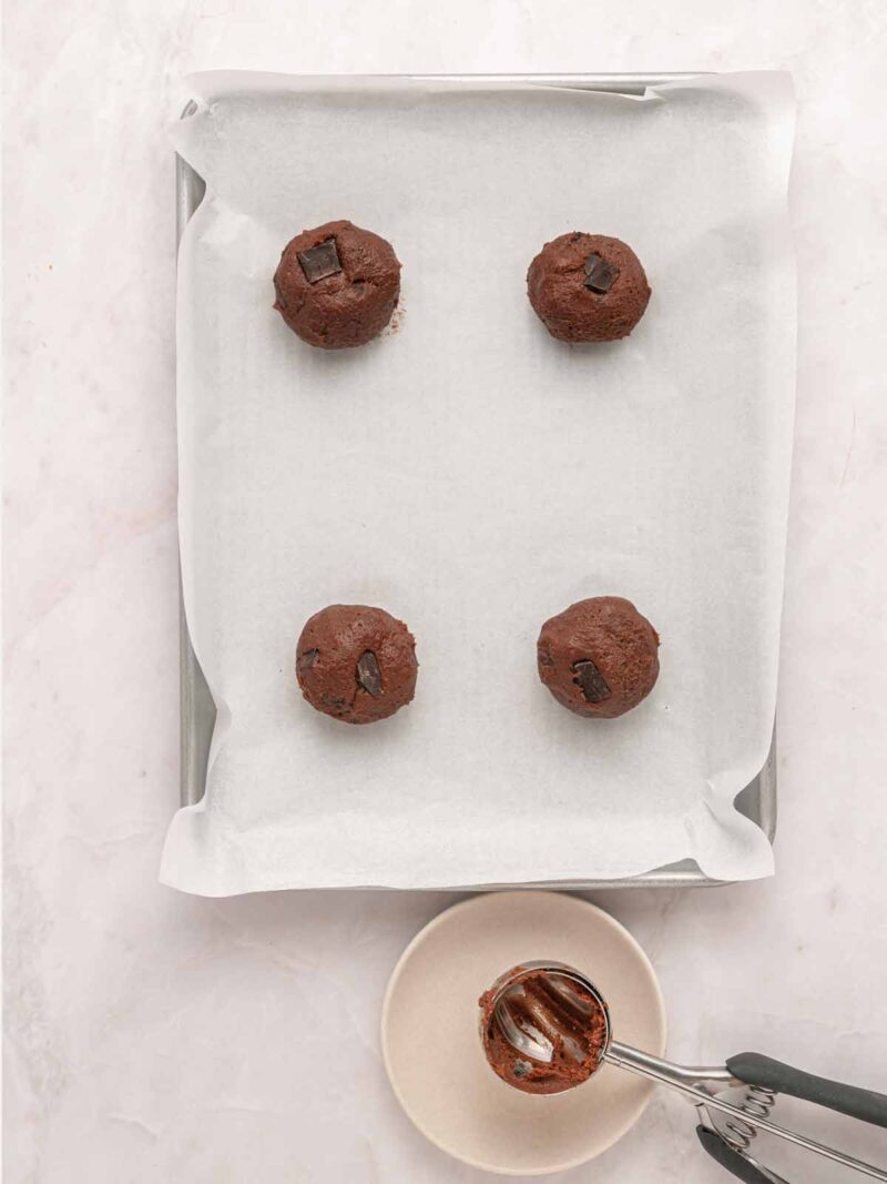 Scooping chocolate cookie dough on a baking sheet.