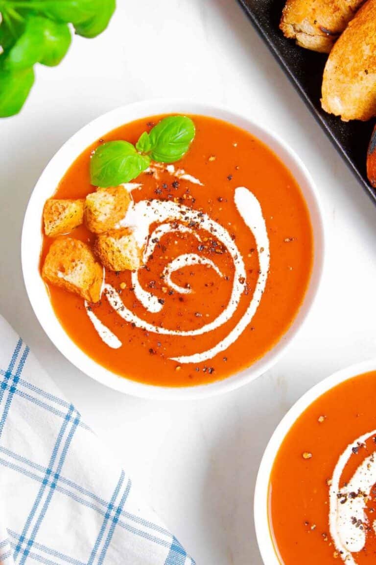 Two white bowls with roasted red pepper and tomato soup, topped with croutons.