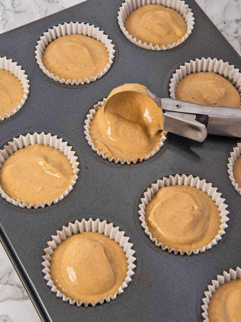 Using a cookie scoop to place cream cheese mixture on top of the cookie crust in the muffin liners.