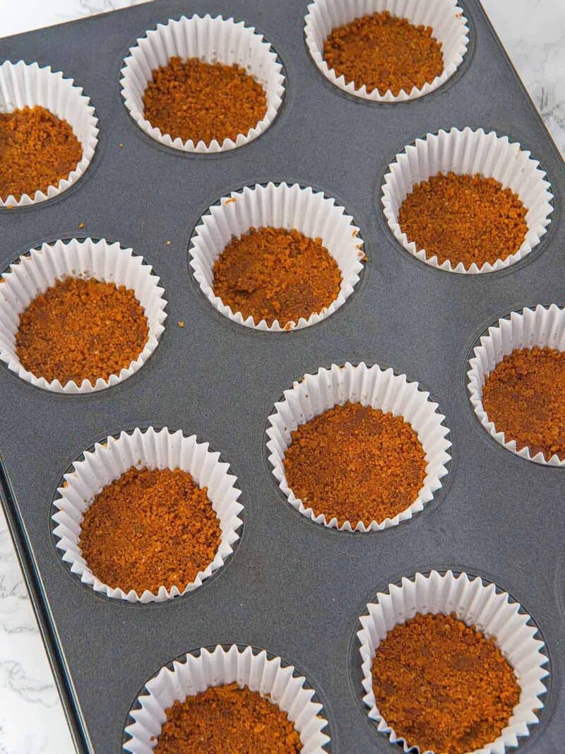 Cookie crust pressed into mini muffin liners in a muffin tin.