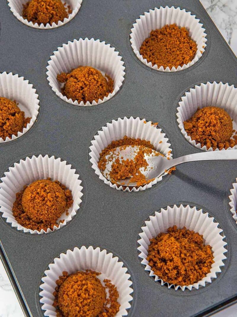 Using a spoon to press the cookie crust into mini muffin liners.