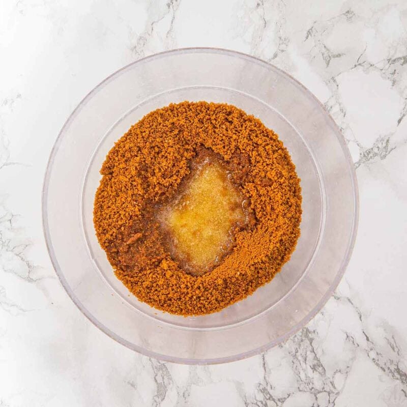 Melted butter added to the biscoff cookie crumbs in a bowl.