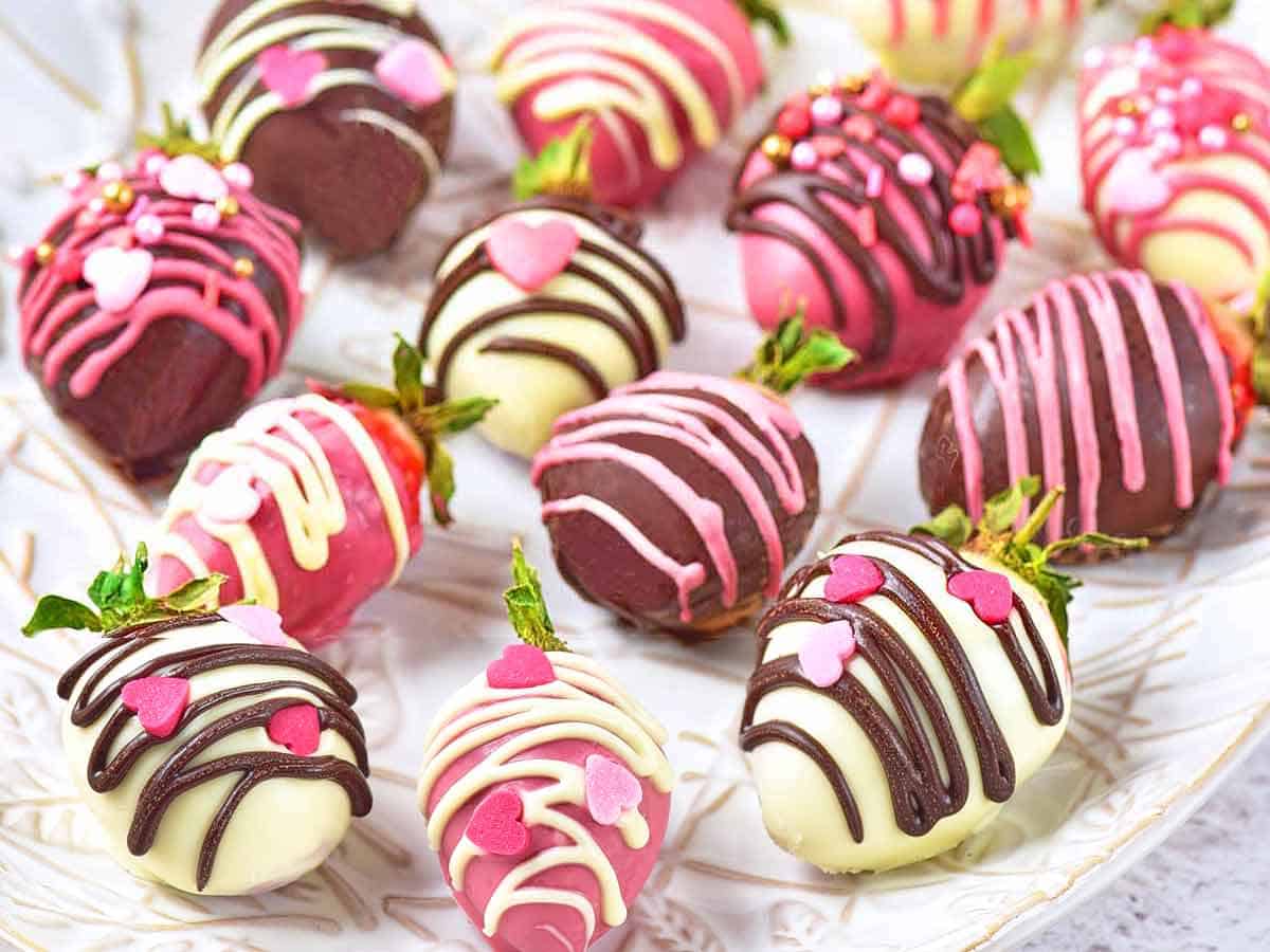 A white serving dish with chocolate strawberries decorated with heart sprinkles.