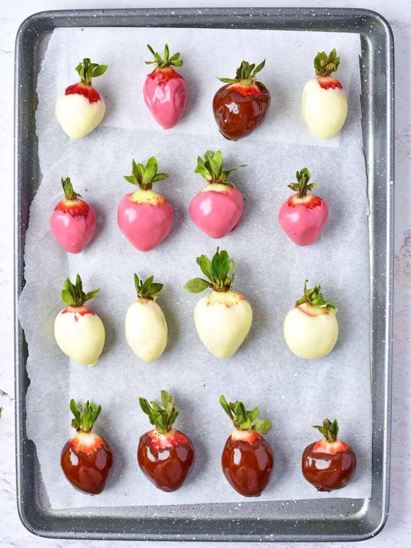 Strawberries dipped in three kinds of chocolate arranged on a parchment lined baking sheet.