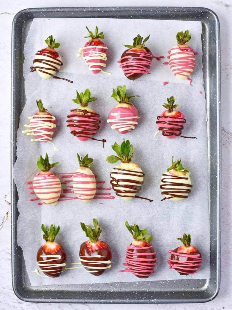 Drizzling strawberries on a parchment lined baking sheet with melted chocolate.