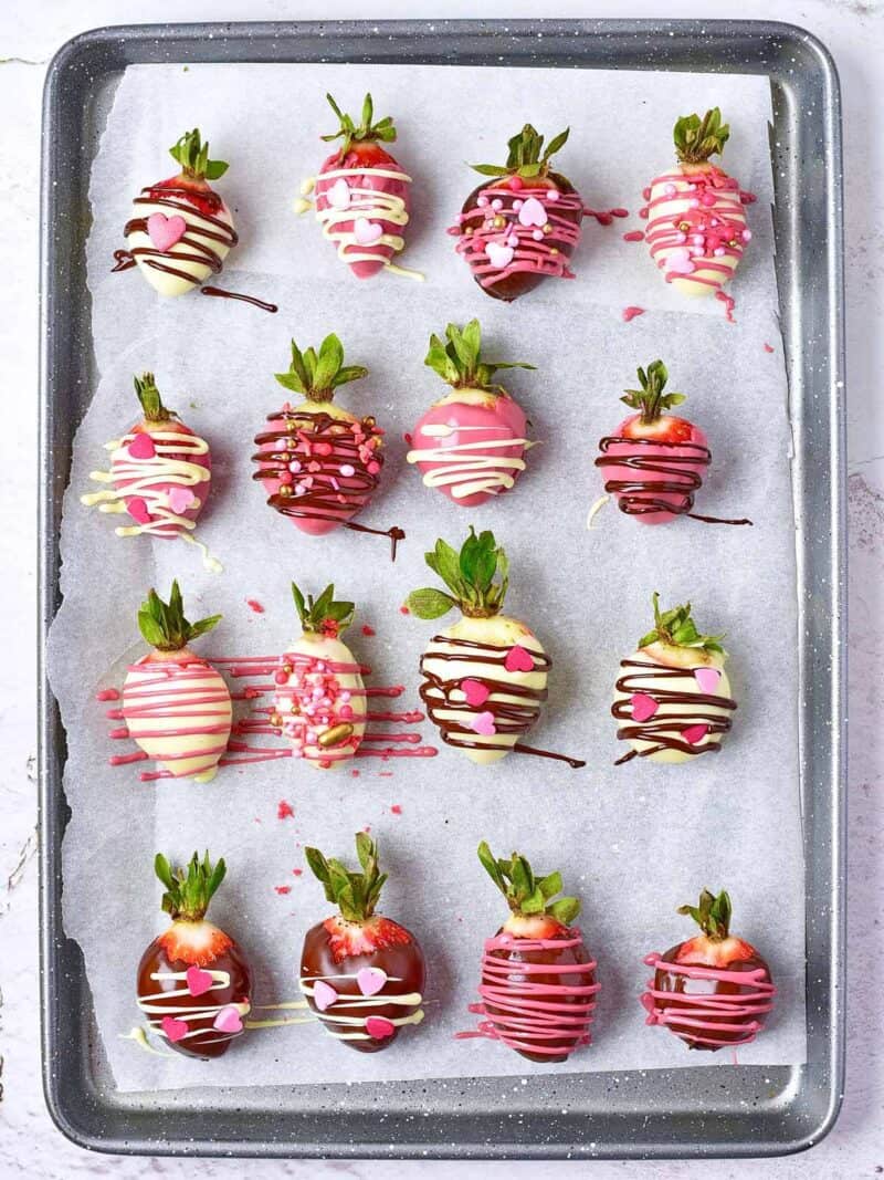 Topping the chocolate covered strawberries with sprinkles on a parchment lined baking sheet.