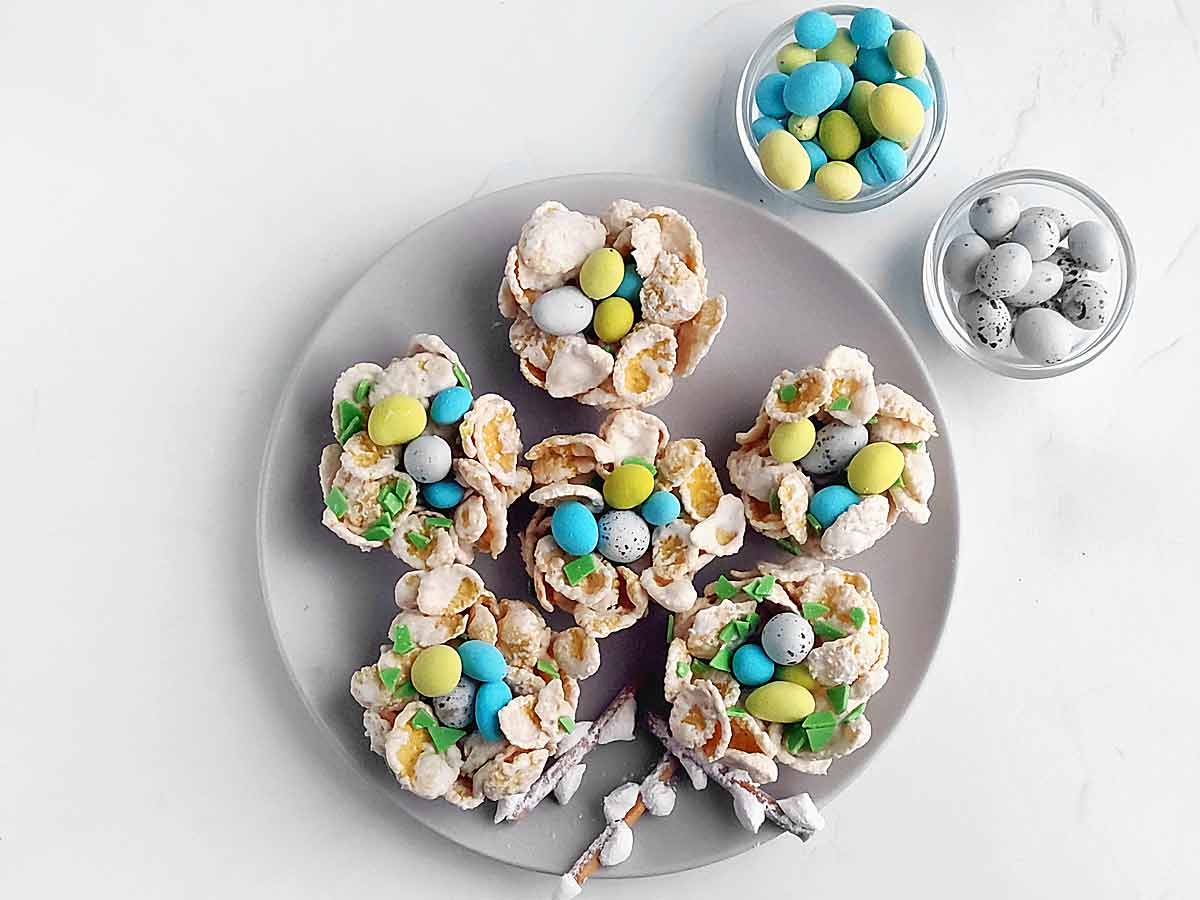 Six Easter birds nest cookies with two bowls of chocolate mini eggs.